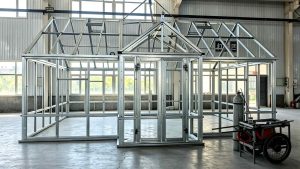 Front gable steel frame of Canadian greenhouse with screen door opening, assembled in workshop.